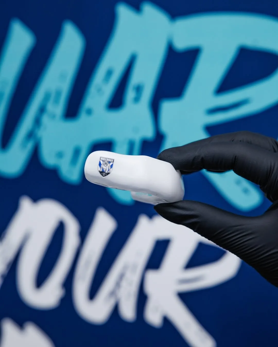A gloved hand holds a white guard printed with the Canterbury-Bankstown Bulldogs logo.