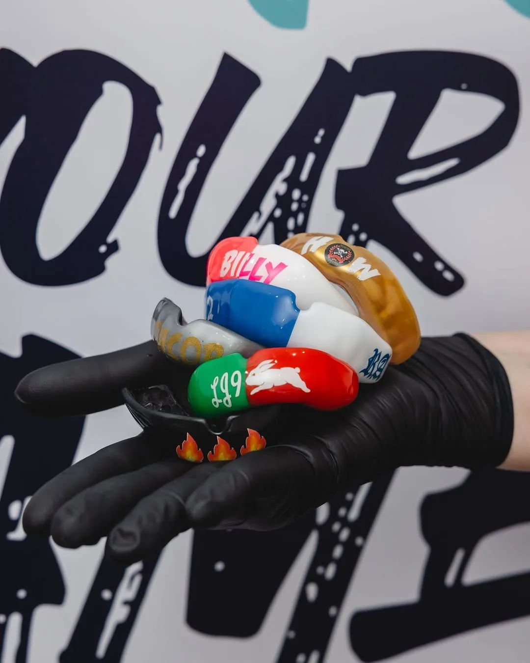 A gloved hand holding a collection of personalised sports mouthguards.