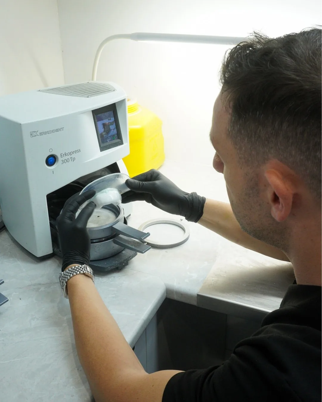 A technician shapes a mouthguard over a dental model using the laboratory's thermoforming machine.