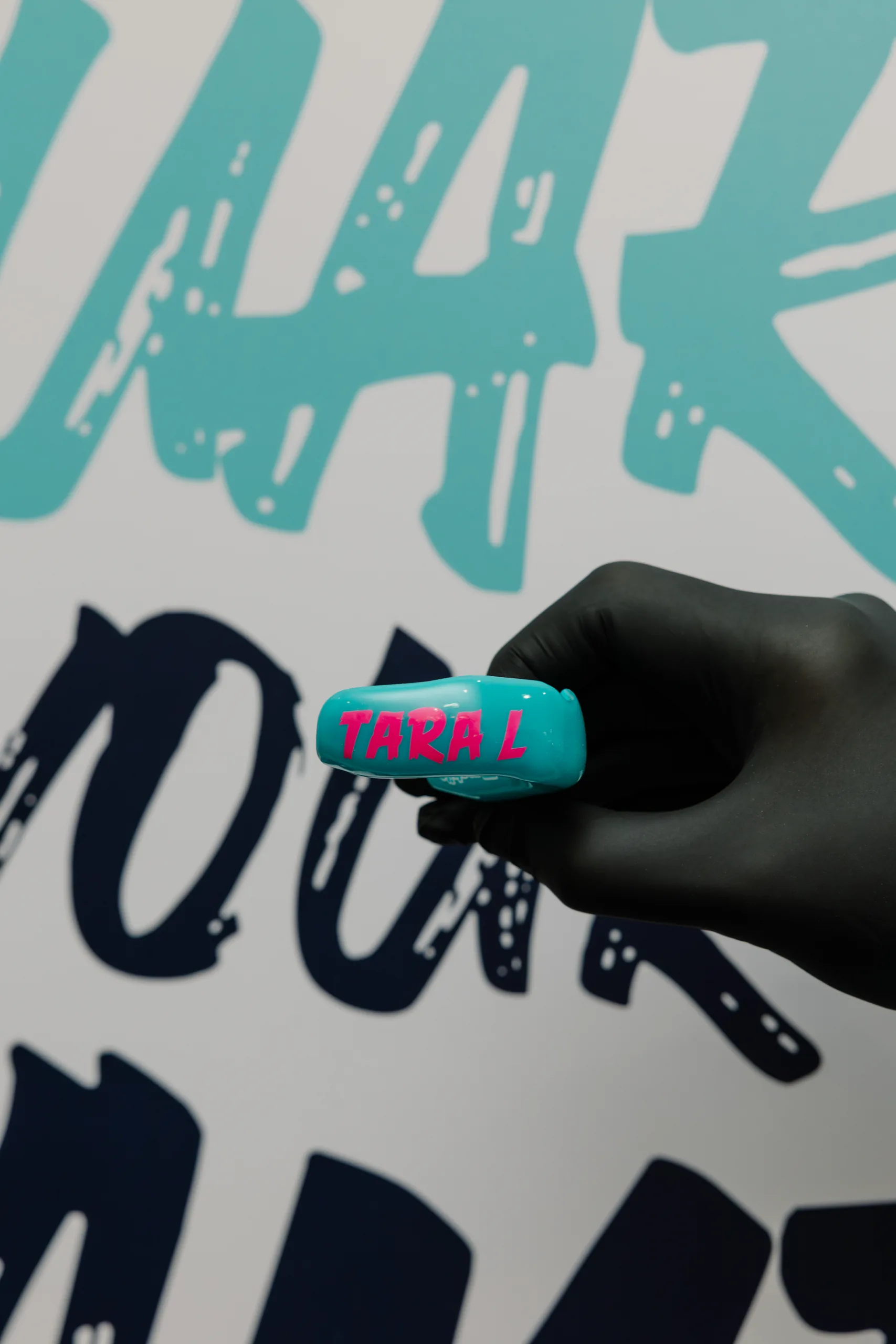 Teal custom mouthguard with pink Tara L lettering, held by a gloved hand.