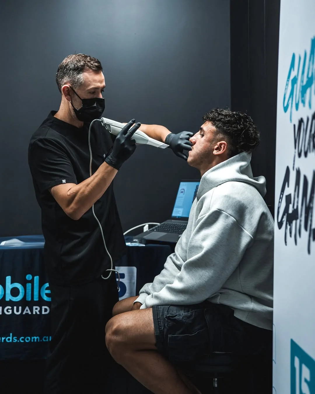 A player in a grey hoodie has his teeth scanned beside the Guard Your Game banner.