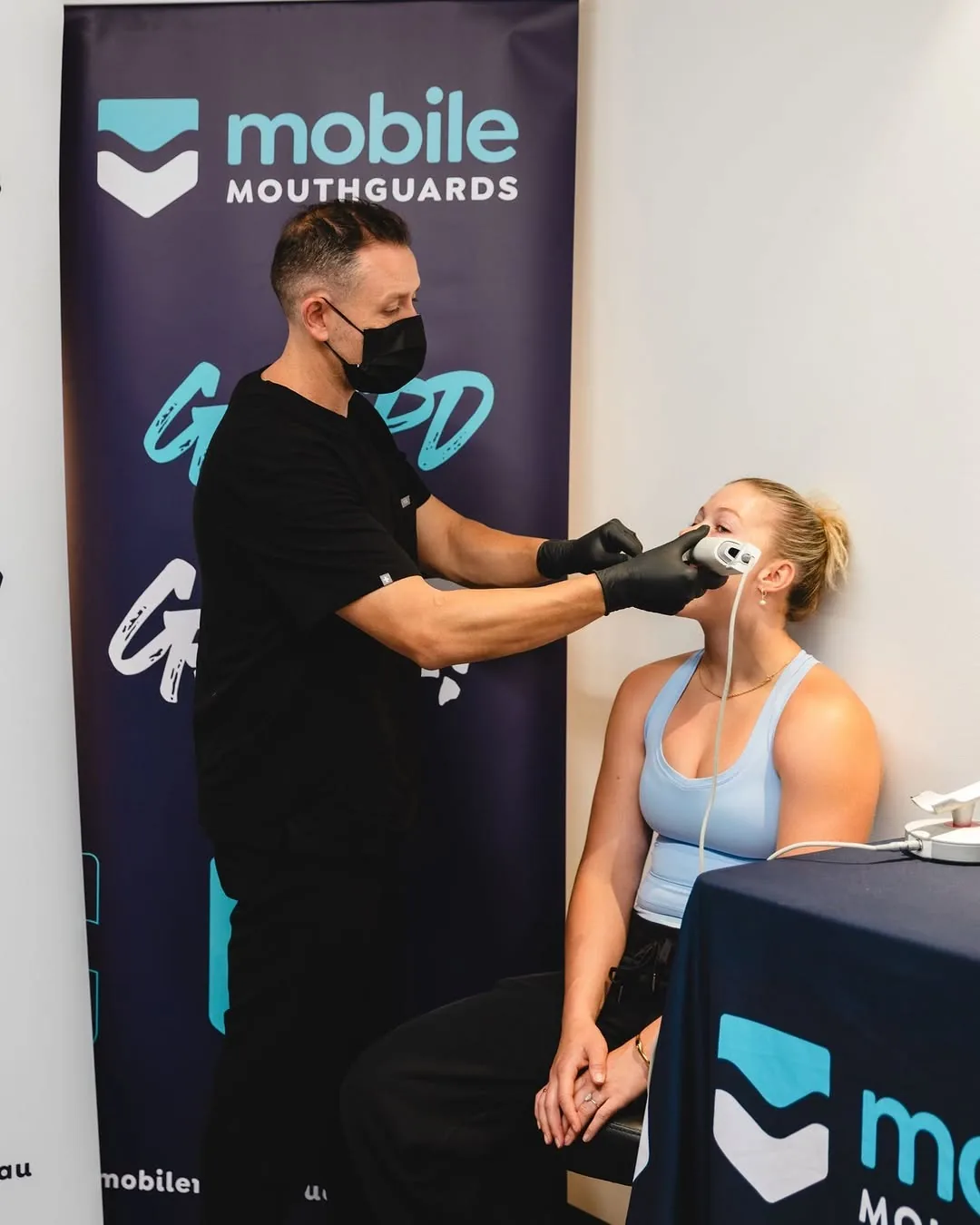 A player sits for her scan while the technician holds the scanner to her teeth, in front of the Mobile Mouthguards banner.